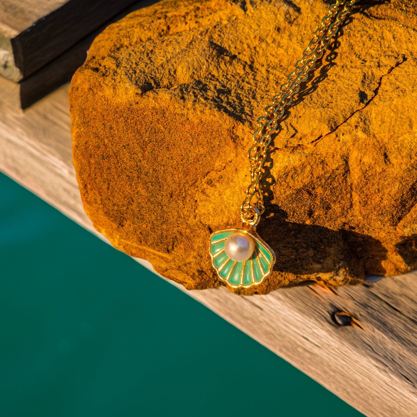 Brown stone with a turquoise shell pearl pendant on a wooden surface next to water.
