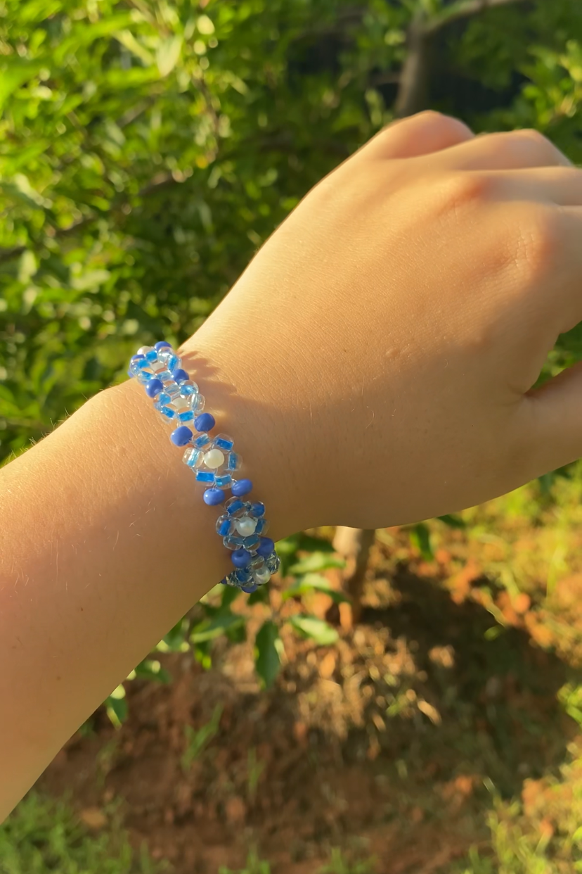 Hand wearing a blue beaded bracelet with a blurred natural background
