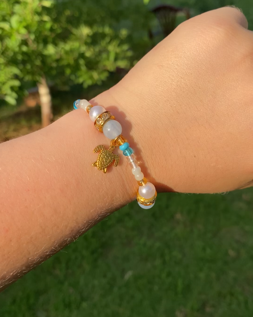 Bracelet with a turtle charm on a wrist against a blurred green outdoor background
